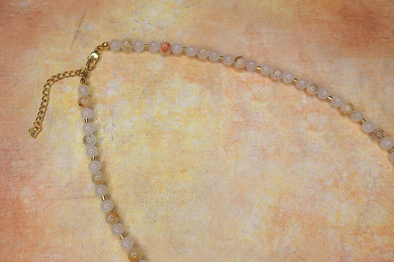 May include: A gold chain necklace with a clasp and a strand of white and light pink beads.