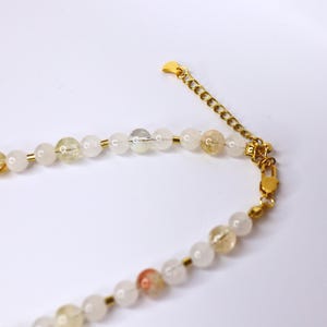May include: A gold chain necklace with white and yellow beads. The necklace has a lobster clasp closure.