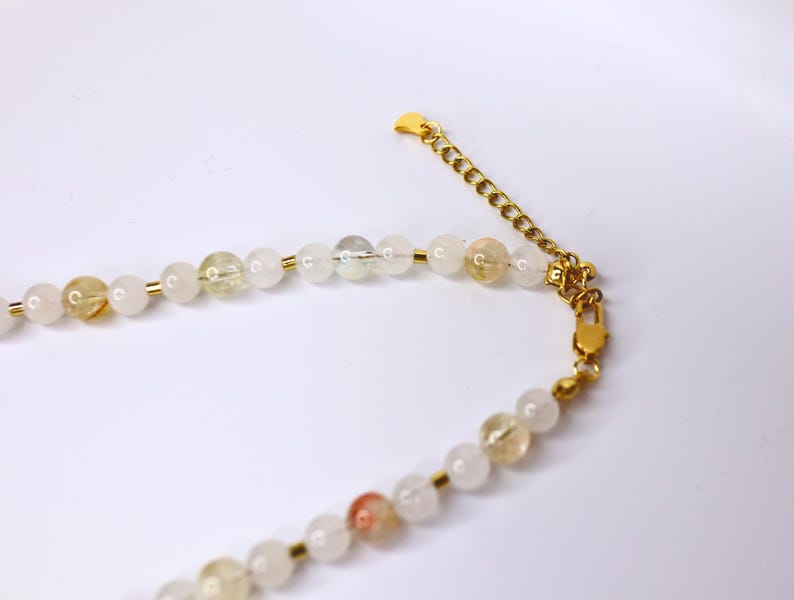 May include: A gold chain necklace with white and yellow beads. The necklace has a lobster clasp closure.