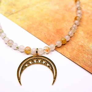 May include: A gold crescent moon pendant necklace with a white and orange gemstone beaded chain.