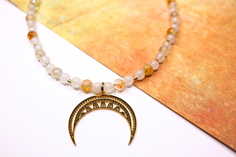 May include: A gold crescent moon pendant necklace with a white and orange gemstone beaded chain.