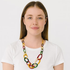 May include: A vibrant chain necklace featuring large oval links in red, green, yellow, and cream. The necklace is worn over a white t-shirt. The necklace is a bold statement piece, with each link approximately 4 cm in length.