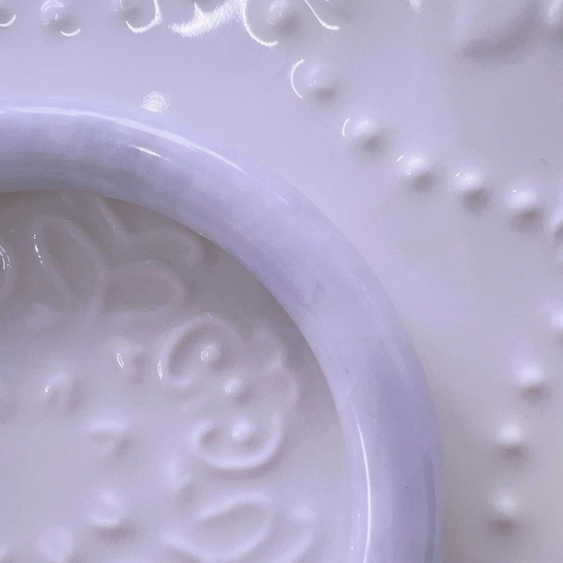May include: A smooth, polished lavender-colored bangle bracelet with a rounded profile. The bangle features a consistent, solid light purple hue with subtle variations in tone throughout its circular structure, showcasing a clean and simple design.