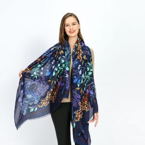 May include: A navy blue scarf with a floral print in shades of green, purple, orange, and yellow. The scarf is made of a soft, lightweight fabric and is perfect for adding a touch of color to any outfit.