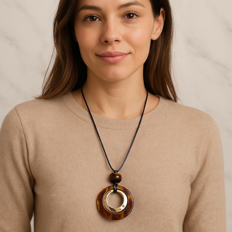 May include: A pendant necklace with a large, tortoiseshell-effect ring and a gold-coloured inner ring. The necklace has a black cord and a small, dark brown bead above the ring.