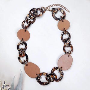 Puede incluir: Un collar de cadena con estampado marrón y negro con grandes colgantes ovalados marrones.