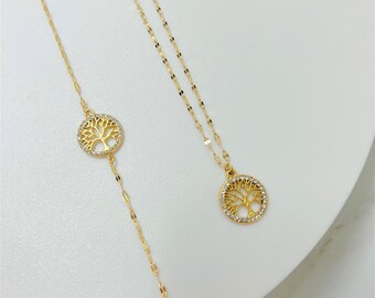 May include: Two gold-colored necklaces with tree of life pendants. One necklace has a longer chain with a circular pendant, and the other has a shorter chain. The pendants are adorned with small, clear crystals.