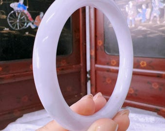May include: A smooth, solid lavender-coloured bangle bracelet with a rounded profile. The bangle has a polished, semi-translucent appearance and a consistent circular shape, showcasing a soft purple hue throughout the entire piece of jewellery.