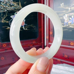 May include: A smooth, polished, translucent white jade bangle bracelet with a rounded profile. The circular jewelry piece features a consistent, solid pale color throughout its entire structure, showcasing a clean and simple design.
