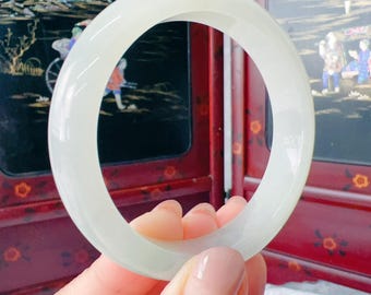 May include: A smooth, polished, translucent white jade bangle bracelet with a rounded profile. The circular jewellery piece features a consistent, solid pale colour throughout its entire structure, showcasing a clean and simple design.