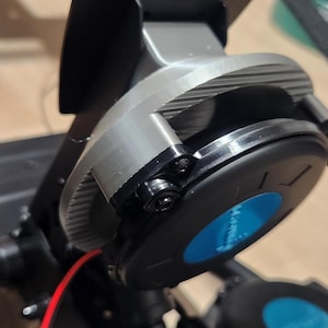 Puede incluir: Primer plano de un mecanismo de giro de auriculares plateado y negro con un acento azul. El mecanismo está unido a unos auriculares negros.