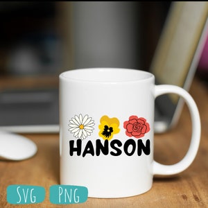 May include: White ceramic mug with a black and white daisy, a yellow pansy, and a red rose graphic. The text "HANSON" is printed in black below the flowers.