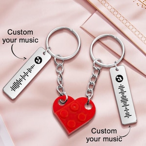 May include: Two silver keychains with a red heart-shaped charm. Each keychain has a rectangular tag with a music waveform and the text "Custom your music". The heart charm is made of red plastic.