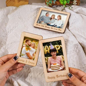 May include: Three rectangular wooden photo frames with light-colored wood grain. One frame features the text "Drive Safe Daddy We Love You" with a family photo. Another displays "James & Emma" with a couple, and the third says "Happy Birthday".