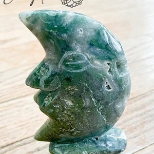 May include: Green agate crescent moon carving with a textured surface. The carving is on a wooden surface. View 3.