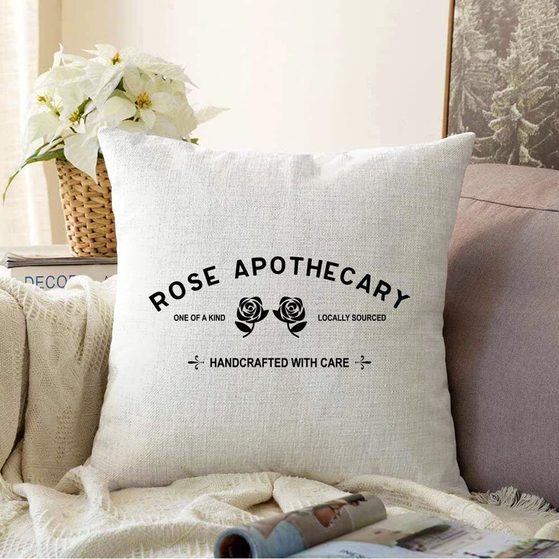 May include: White throw pillow with black text that reads "Rose Apothecary" with two black roses and the text "One of a Kind", "Locally Sourced", and "Handcrafted with Care".