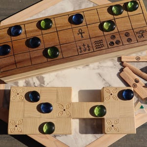 May include: A wooden board game with a brown wooden game board and light wooden game pieces. The game board has a grid pattern with blue and green glass game pieces. The game pieces are arranged on a white and marble-patterned surface.
