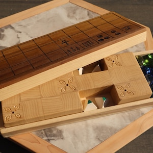 May include: Wooden board game with a dark brown playing surface and a light wood frame. The game includes a compartment with colorful glass game pieces. The game board is open, revealing the game pieces and the interior.