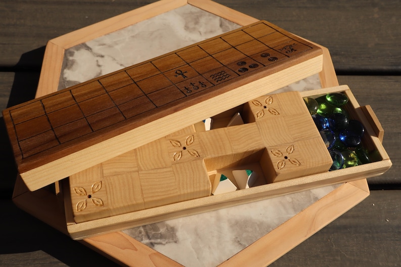May include: Wooden board game with a dark brown playing surface and a light wood frame. The game includes a compartment with colorful glass game pieces. The game board is open, revealing the game pieces and the interior.