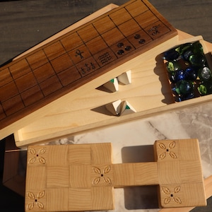 May include: Wooden board game set with a light wood finish. The set includes a rectangular game board with a grid pattern, a tray of glass marbles, and other wooden game pieces. The game board has etched symbols.