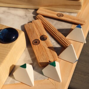 May include: Wooden game pieces and a decorative wooden box. The box has a blue glass stone and carved floral details. The game pieces include small white pyramids with colored tips and wooden sticks with etched designs.