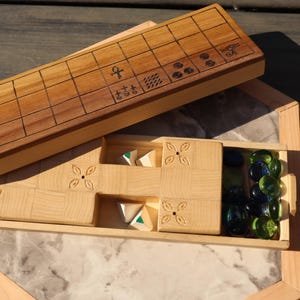 May include: Wooden board game with a light brown finish. The game includes a wooden board with etched lines and symbols, a compartment with game pieces, and a marble-like base. The game pieces are triangular and green and white.