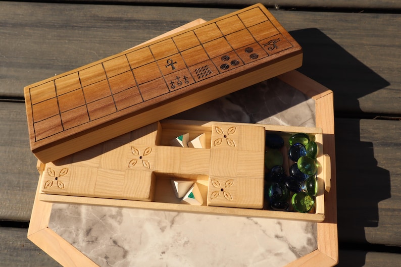 May include: Wooden board game with a light brown finish. The game includes a wooden board with etched lines and symbols, a compartment with game pieces, and a marble-like base. The game pieces are triangular and green and white.
