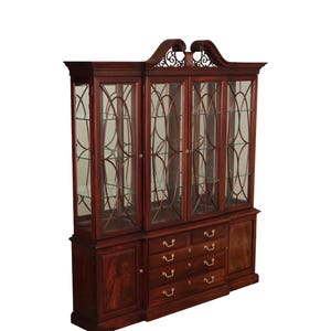May include: A large, dark wood display cabinet with glass doors and shelves. The cabinet has a decorative top and brass drawer pulls. The glass doors have a decorative pattern. The cabinet has multiple drawers and a lower cabinet with a wooden door.