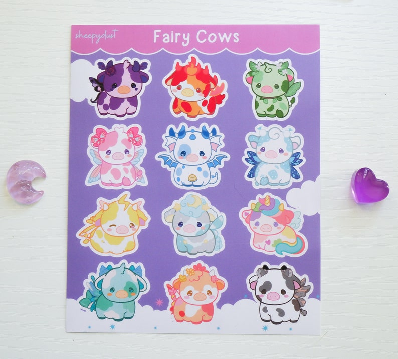 Puede incluir: Una hoja de pegatinas con 12 dise&ntilde;os diferentes de vacas hadas. Cada vaca tiene un esquema de color diferente y caracter&iacute;sticas &uacute;nicas, como alas, cuernos y flores. Las pegatinas est&aacute;n impresas sobre un fondo morado con nubes blancas.