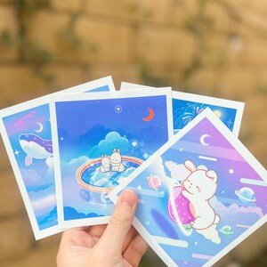 Op de afbeelding: Set van vier ge&iuml;llustreerde kaarten met schattige cartoon konijnen in een dromerige nachtelijke hemel. De kaarten bevatten een halve maan, sterren en een verscheidenheid aan pastelkleuren.