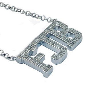 May include: A silver chain necklace with a pendant that spells out "FJB" in block letters. The letters are covered in small, clear stones.
