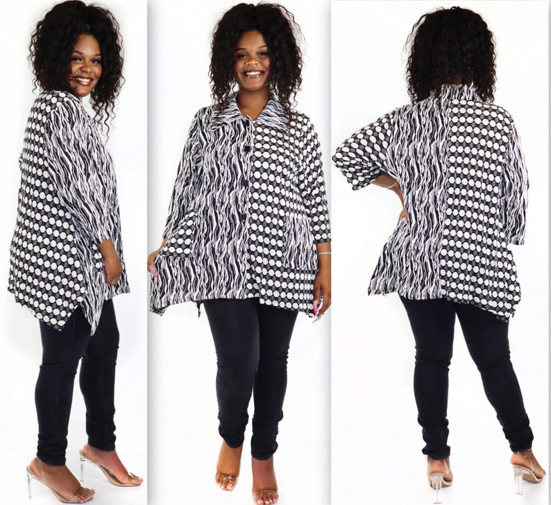 May include: A black and white patterned shirt with a button-up front and long sleeves. The shirt has a loose fit and a slightly asymmetrical hemline. The model is wearing black trousers and clear heeled sandals.
