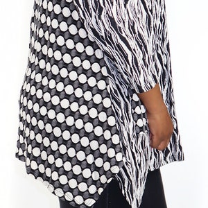May include: A woman wearing a black and white patterned blouse with a black and white zebra print on one side and a black and white polka dot pattern on the other side. She is wearing black jeans and clear heeled sandals.