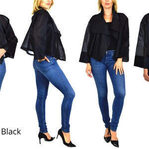 May include: A black cropped jacket with a draped collar and sheer sleeves. The jacket is worn over a pair of blue jeans.