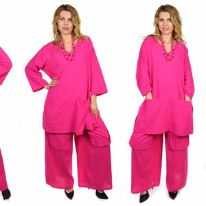May include: A pink two-piece outfit with a long-sleeved top and wide-leg pants. The top has a V-neckline and pockets on the sides. The pants have pockets on the sides and are loose-fitting.