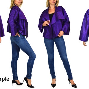 May include: A purple, cropped, open-front jacket with long sleeves. The jacket is made of a silky fabric and has a draped design. The model is wearing blue jeans and black heels.