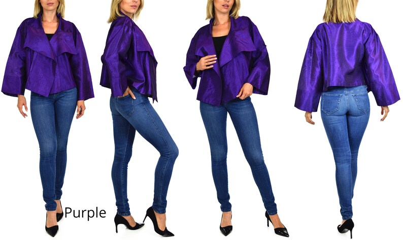 May include: A purple, cropped, open-front jacket with long sleeves. The jacket is made of a silky fabric and has a draped design. The model is wearing blue jeans and black heels.