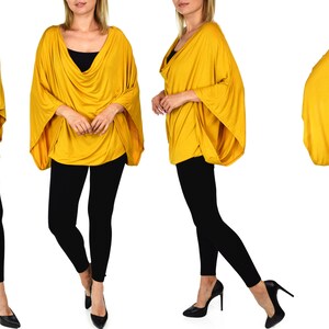 K&ouml;nnte beinhalten: Ein locker sitzendes, lang&auml;rmliges Oberteil in Senfgelb mit einem Schalkragen. Das Oberteil wird an einem Model gezeigt, das schwarze Leggings und hohe Abs&auml;tze tr&auml;gt.