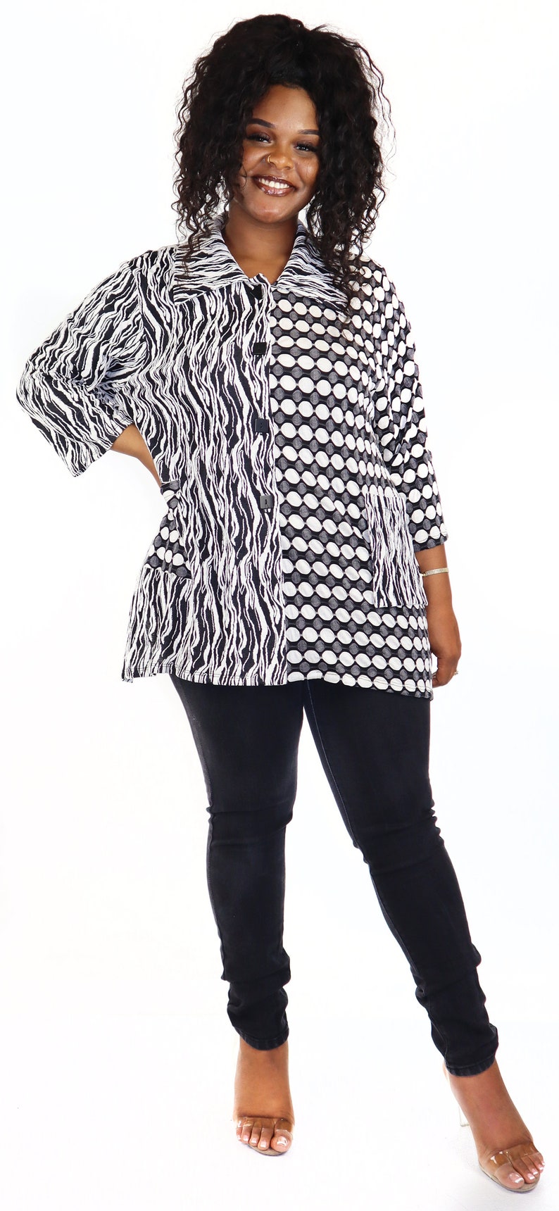 May include: A black and white patterned blouse with a button fastening. The blouse features a zebra-like pattern on one side and a polka dot pattern on the other. The model is wearing black jeans and clear heeled sandals.
