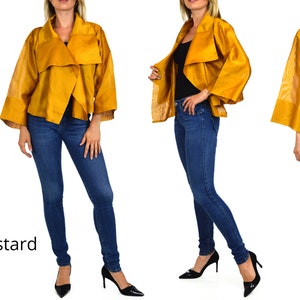 May include: A mustard yellow cropped jacket with a draped collar and wide sleeves. The jacket is worn over a black top and blue jeans.