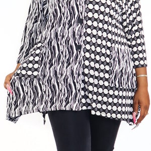 May include: A black and white patterned tunic with a long sleeve and a button-up front. The tunic has a wavy pattern on one side and a polka dot pattern on the other side. The model is wearing black leggings and clear heels.