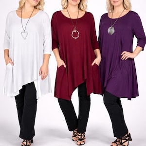May include: Three women modeling asymmetrical tunic tops in white, burgundy, and purple, paired with black pants. Each outfit is accessorized with a silver pendant necklace. The tunics have pockets and three-quarter sleeves.