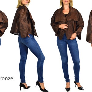 May include: A bronze-colored jacket with a draped collar and long sleeves. The jacket is worn by a model who is wearing blue jeans and black heels. The word "Bronze" is written in white text below the model.