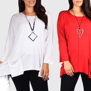 May include: Two women wearing long-sleeved tops with asymmetrical hems. The top on the left is white with a silver chain and square pendant necklace. The top on the right is red with a silver heart pendant necklace.