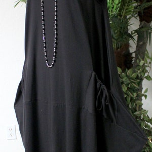 May include: A black sleeveless dress with a scoop neck and a long, flowing skirt. The dress has a drawstring detail at the sides and a beaded necklace.