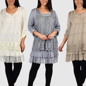 Puede incluir: Tres blusas de manga larga, de capas y con ribete de encaje en marfil, gris y beige. Cada blusa tiene un cierre de botón en el cuello y un dobladillo con volantes superpuestos.