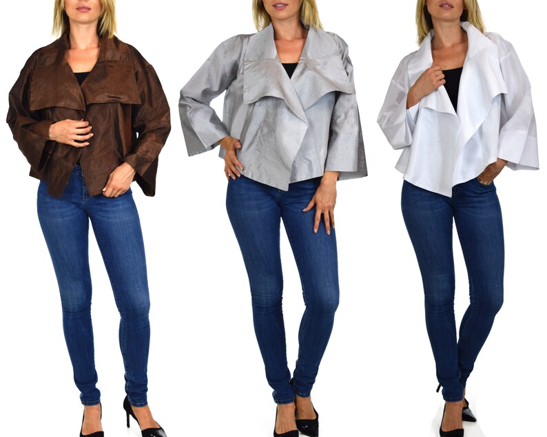 May include: Three women are wearing different colored jackets. The jackets are all the same style, with a long, flowing collar and a loose fit. The jackets are made of a soft, silky material. The women are all wearing blue jeans.