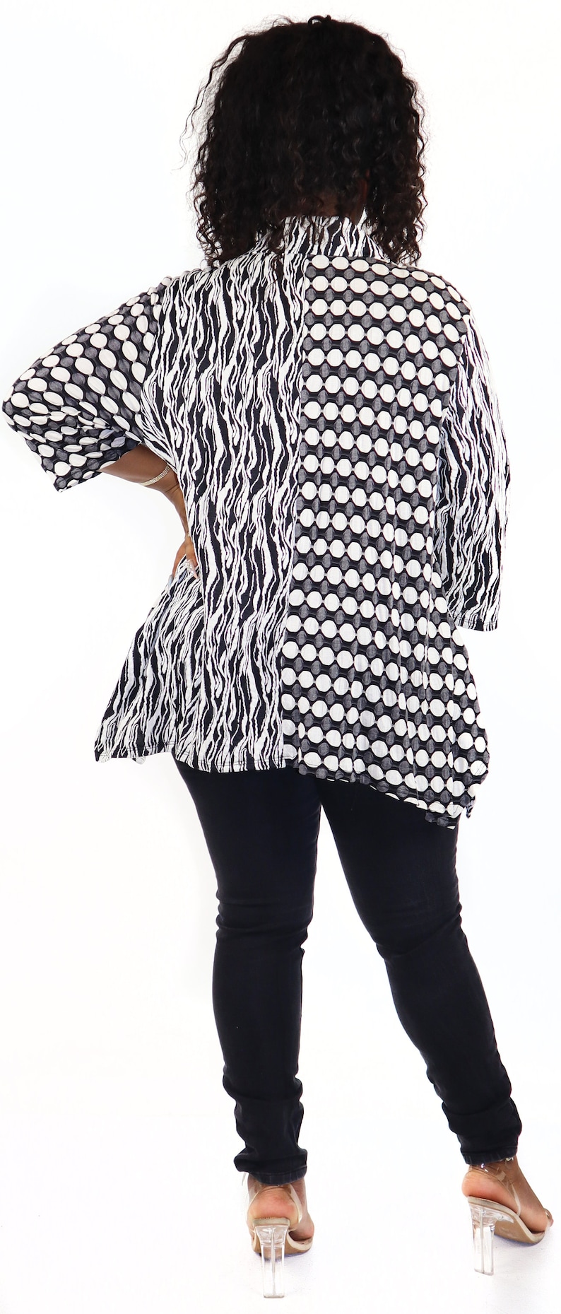 May include: A black and white patterned blouse with a loose fit and a high neckline. The blouse is worn with black jeans and clear heeled sandals.