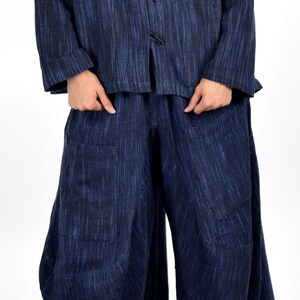 May include: A blue linen jacket with a mandarin collar and a row of buttons down the front. The jacket is paired with matching blue linen pants.