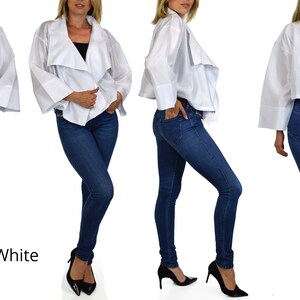 May include: A white, lightweight, cropped jacket with a draped, asymmetrical design. The jacket has long sleeves with wide cuffs and a relaxed fit. The model is wearing the jacket with blue jeans and black heels.